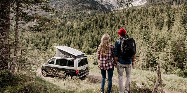 Pärchen genießt den Ausblick Richtung Berge und Vanever Camper