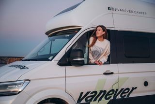 Eine Frau schaut bei Sonnenuntergang aus dem Camperfenster