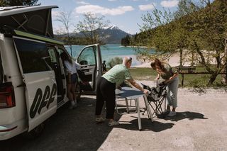 Drei Frauen bereiten den Tisch neben ihrem Off Camper vor, der direkt am Ufer des Walchensees steht